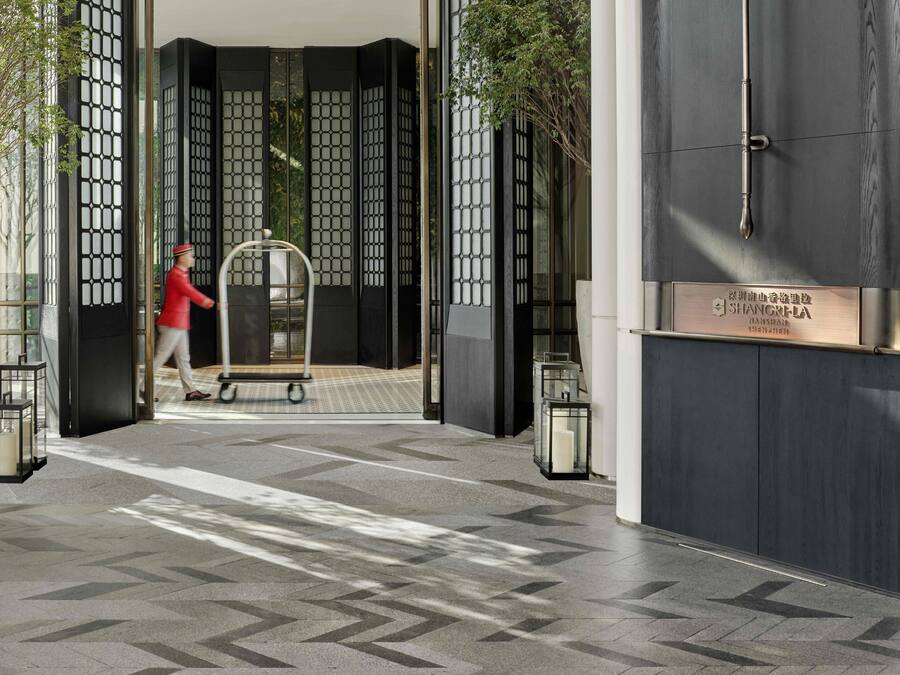 A hotel entrance with a modern design, featuring a large glass door, a metal gate, and a signboard.