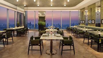 A restaurant with multiple tables and chairs, large windows with a city view, and a modern interior design.