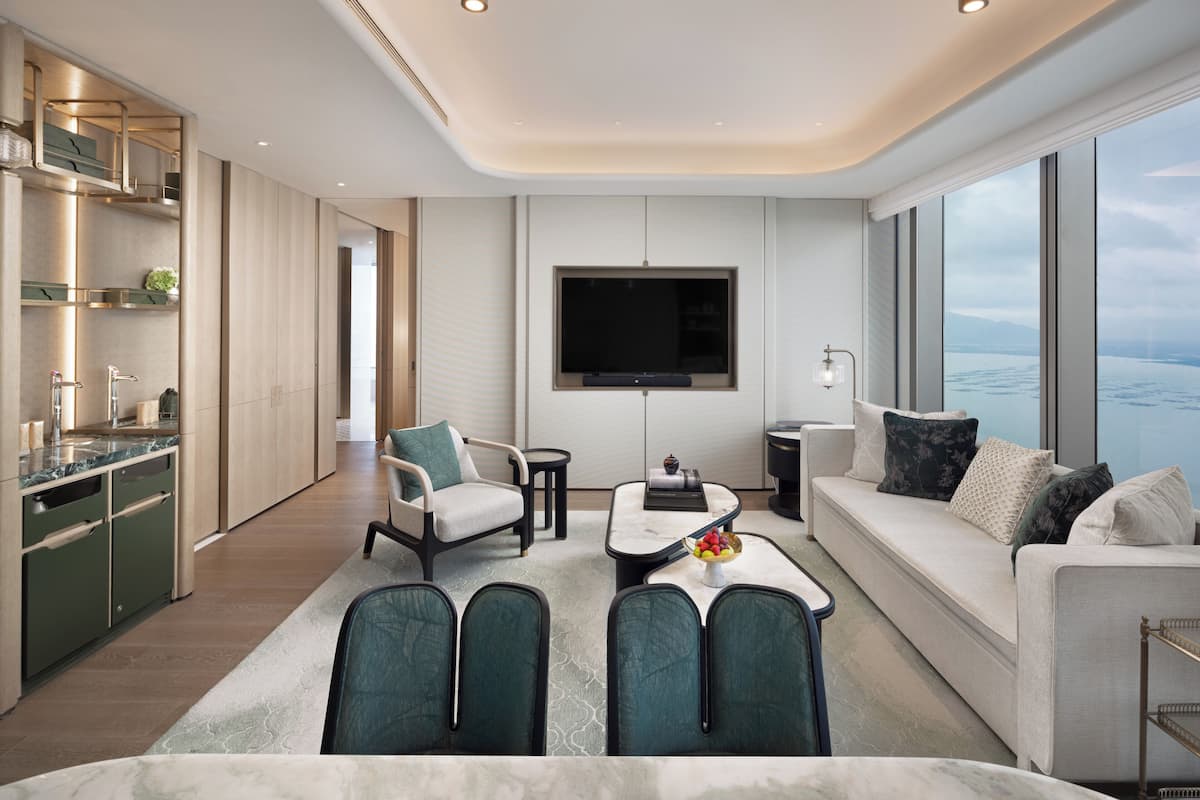 A modern hotel room with a kitchen, seating area, and a large window offering a view of the sea.