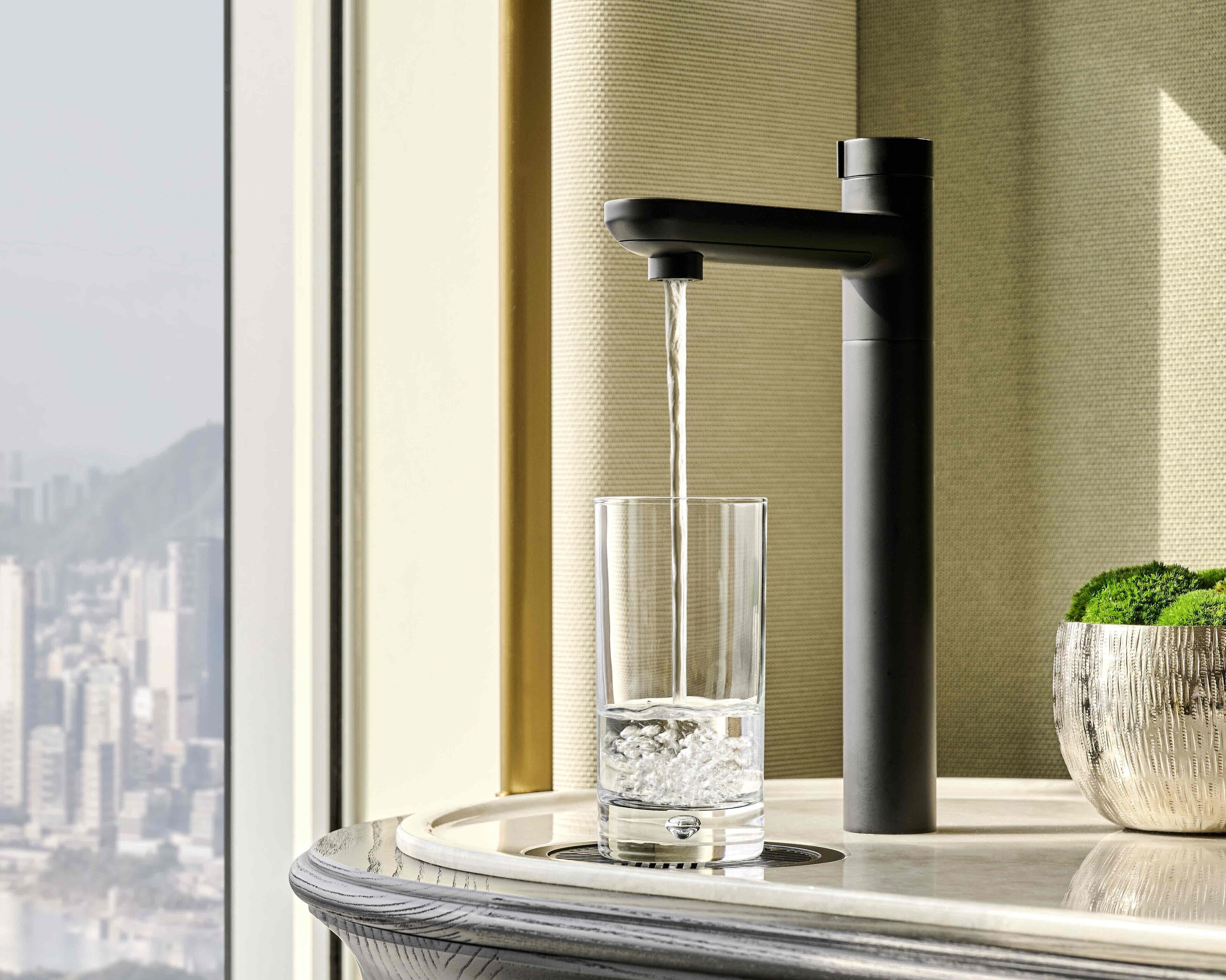 Un baño moderno con un grifo negro, un vaso de agua y una planta en maceta.