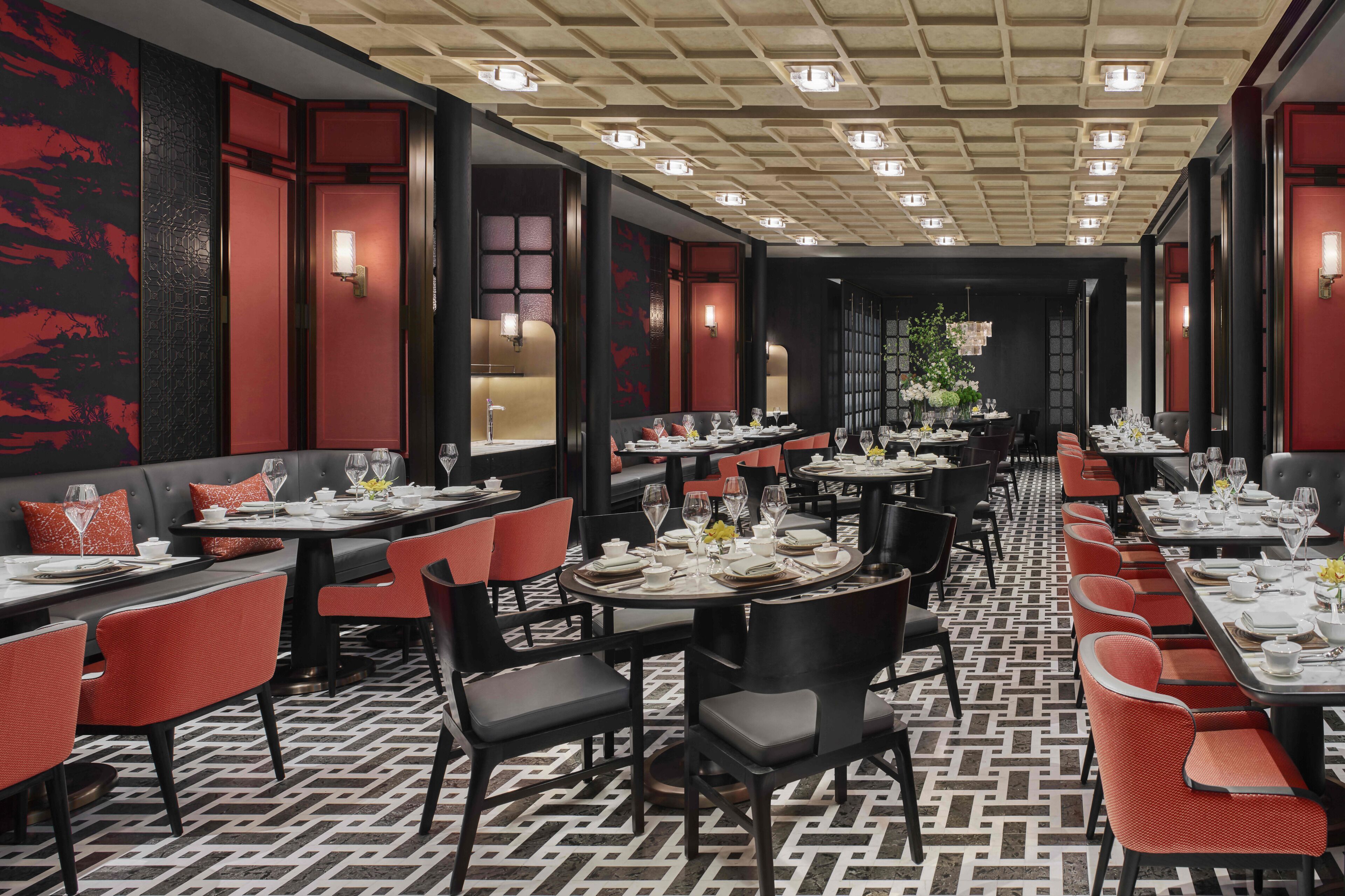 Ein Restaurant mit mehreren Tischen und Stühlen, einem gemusterten Boden und roten und schwarzen Dekorationselementen.