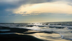 A beach with waves, a cloudy sky, and a sunset.