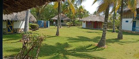 Un resort tropical con cabañas de techo de paja, palmeras y un césped bien cuidado.