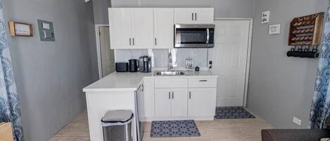 A compact kitchen with white cabinets, a stainless steel microwave, and a coffee machine.