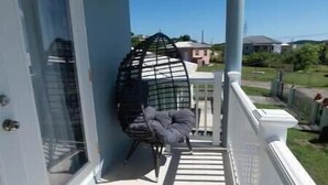 A balcony with a white railing, a glass door, and a black chair. - De ja Blue (Saint George)