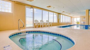 Una piscina interior con agua cristalina azul, rodeada de paredes color beige y ventanas amplias.