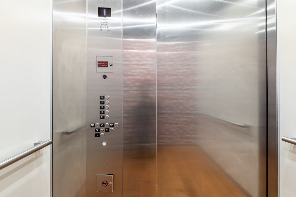 An elevator interior with a control panel, emergency operation button, and a no-smoking sign.
