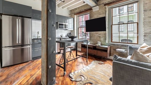A modern kitchen with stainless steel appliances, a bar area, and a large window providing a view of the city.