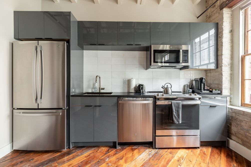A modern kitchen with stainless steel appliances, grey cabinets, and a wooden floor.