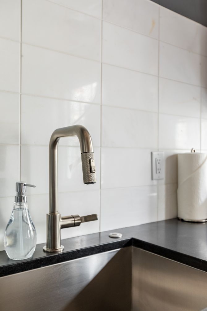 A modern kitchen with a stainless steel faucet, a clear glass bottle, and a black countertop.