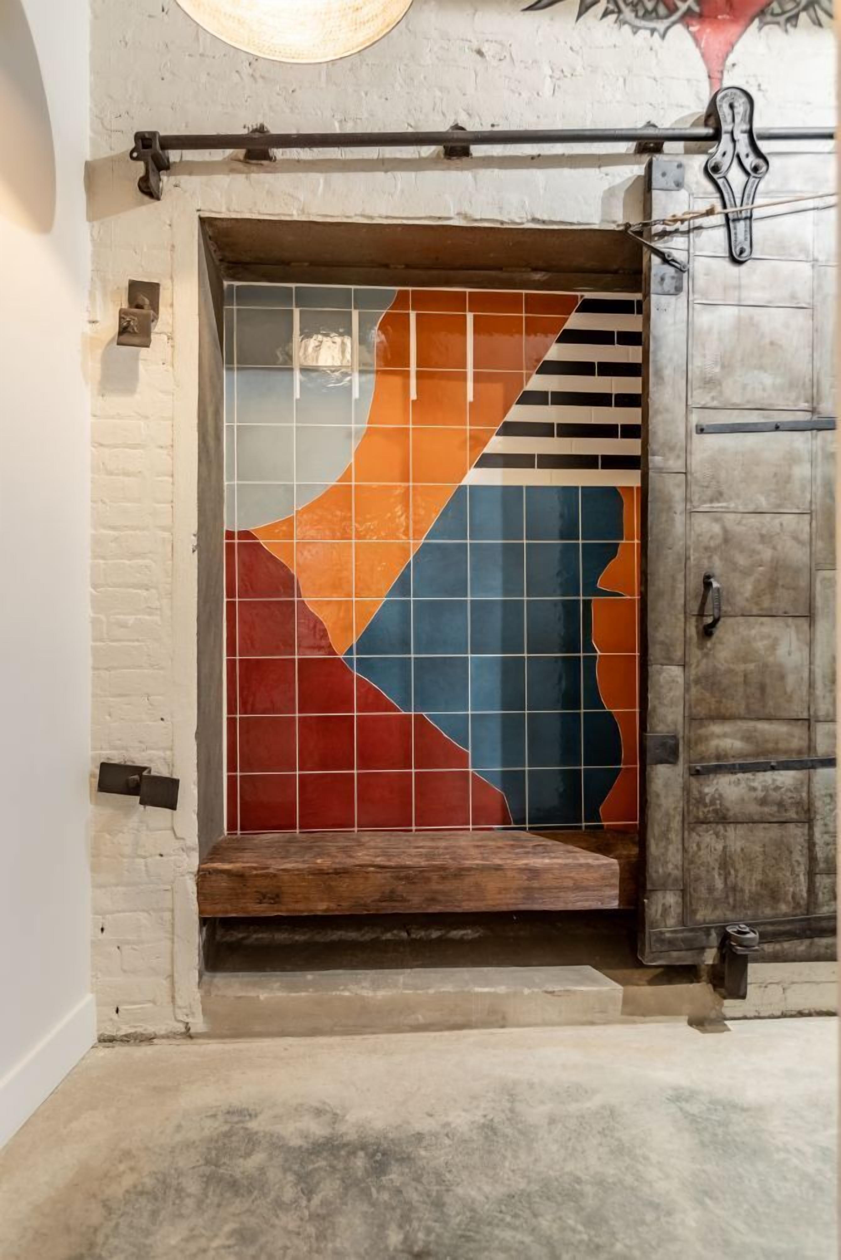 A room with a tiled wall featuring geometric patterns, a wooden bench, and a metal cabinet.