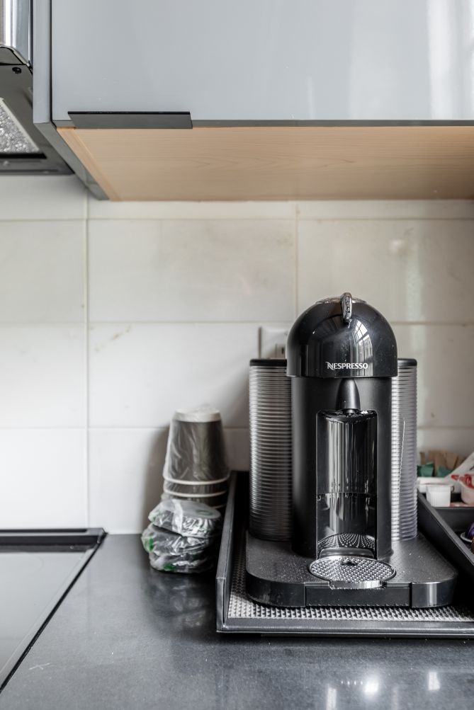 Una cafetera Nespresso sobre una encimera de cocina con salpicadero de azulejos.