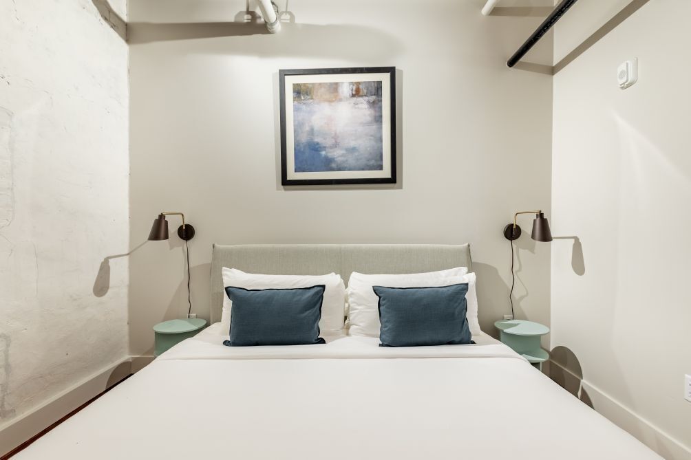Un dormitorio con una cama, dos mesitas de noche, una lámpara de pared y un cuadro enmarcado sobre la cama.