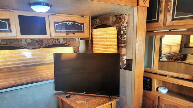 Een ruimtelijk ingericht RV-interieur met een televisie op een houten standaard, een klein tafeltje en een prullenbak.