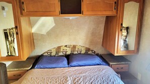 Een compact interieur van een camper, met een bed, opbergkasten en een kitchenette.