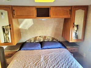 Un intérieur de camping-car compact comprenant un lit, des placards de rangement et un coin cuisine.