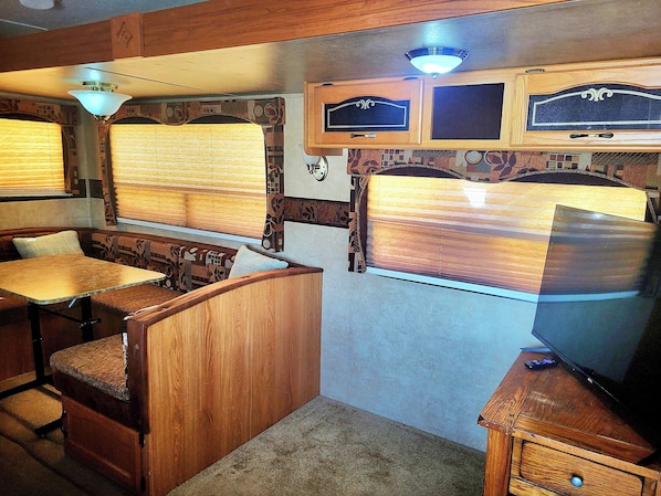 Quarto compacto com mesa e banco de madeira, televisão e ventoinha no teto.