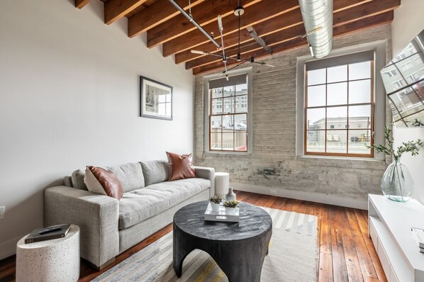 A modern living room with a grey sofa, a round coffee table, and a large window with a city view.