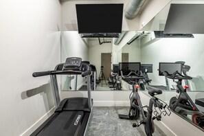 A gym with a treadmill, stationary bikes, and a mirrored wall.