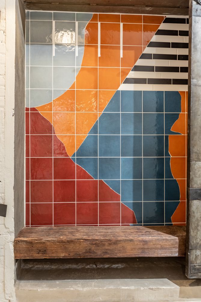 A tiled wall with geometric patterns and a wooden bench.