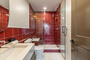 A modern bathroom with a glass shower enclosure, a white toilet, and a vanity with a towel and a bottle.