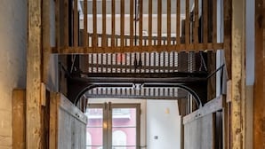 Un pasillo estrecho con puertas de madera y una verja metálica al final.