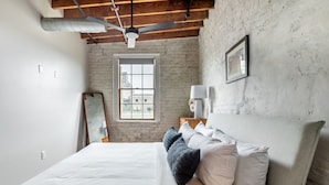 Un dormitorio con una cama grande, un ventilador de techo, una ventana y una lámpara de pared.
