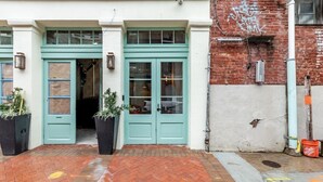 A building with teal double doors, a brick pathway, and a brick wall with graffiti.