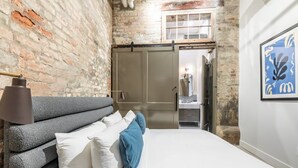 A bedroom with a brick wall, a bed with white and blue bedding, a lamp, and a framed artwork. - Historic Charm Meets Luxury in This Central Warehouse Retreat (New Orleans)