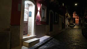 A narrow cobblestone street at night with a building featuring a red facade, a door with a glass panel, and a small set of steps leading to the entrance. - Vacation home (Historical Center) CATANIA (Catania)
