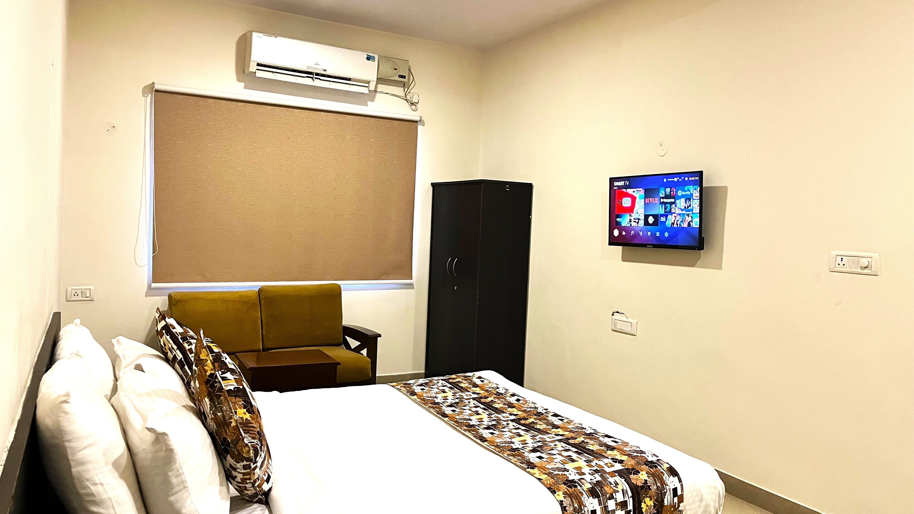 Een hotelkamer met een bed, een slaapbank, een airconditioner, een televisie en een kledingkast.