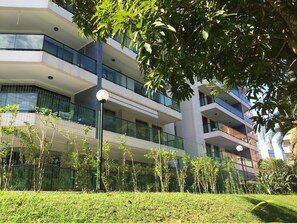 A modern multi-story building with balconies, surrounded by greenery and a fence. - Riviera: M4 Giardino 44A, frente Praia, 4Dorms, 3Banh, 2Gar, Varanda Gourmet com Churrasqueira (Bertioga)
