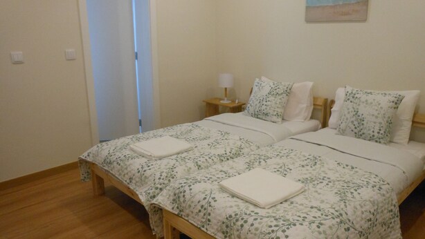 Un dormitorio con cama de madera, dos almohadas, una mesita de noche con lámpara y un cuadro en la pared.