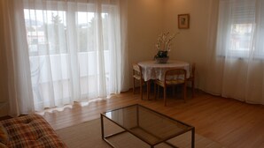 Una sala de estar con una mesa de centro de vidrio, una mesa de comedor con sillas, cortinas translúcidas y un cuadro en la pared.