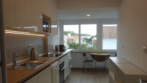 Una cocina moderna con horno integrado, hervidor y cafetera. Se ve una ventana con vistas a casas y árboles.