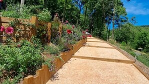 Ein Kiesweg, der von Holzbordüren und üppigem Grün gesäumt wird, führt durch eine parkähnliche Anlage.