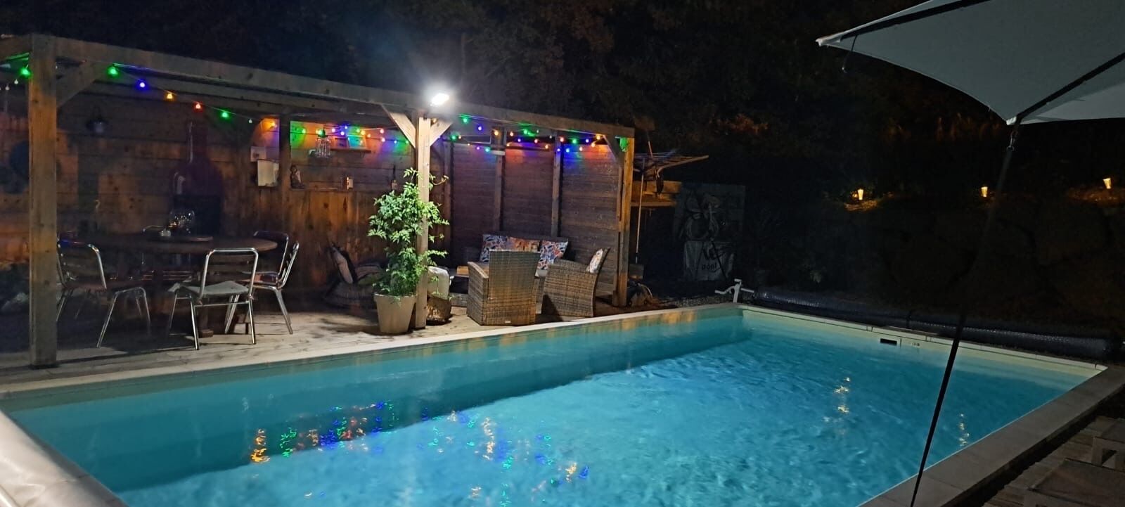 A swimming pool with a wooden deck, outdoor seating, and string lights.