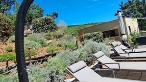 Eine Holzterrasse mit Liegestühlen und einer außergewöhnlichen, schwarzen Skulptur.