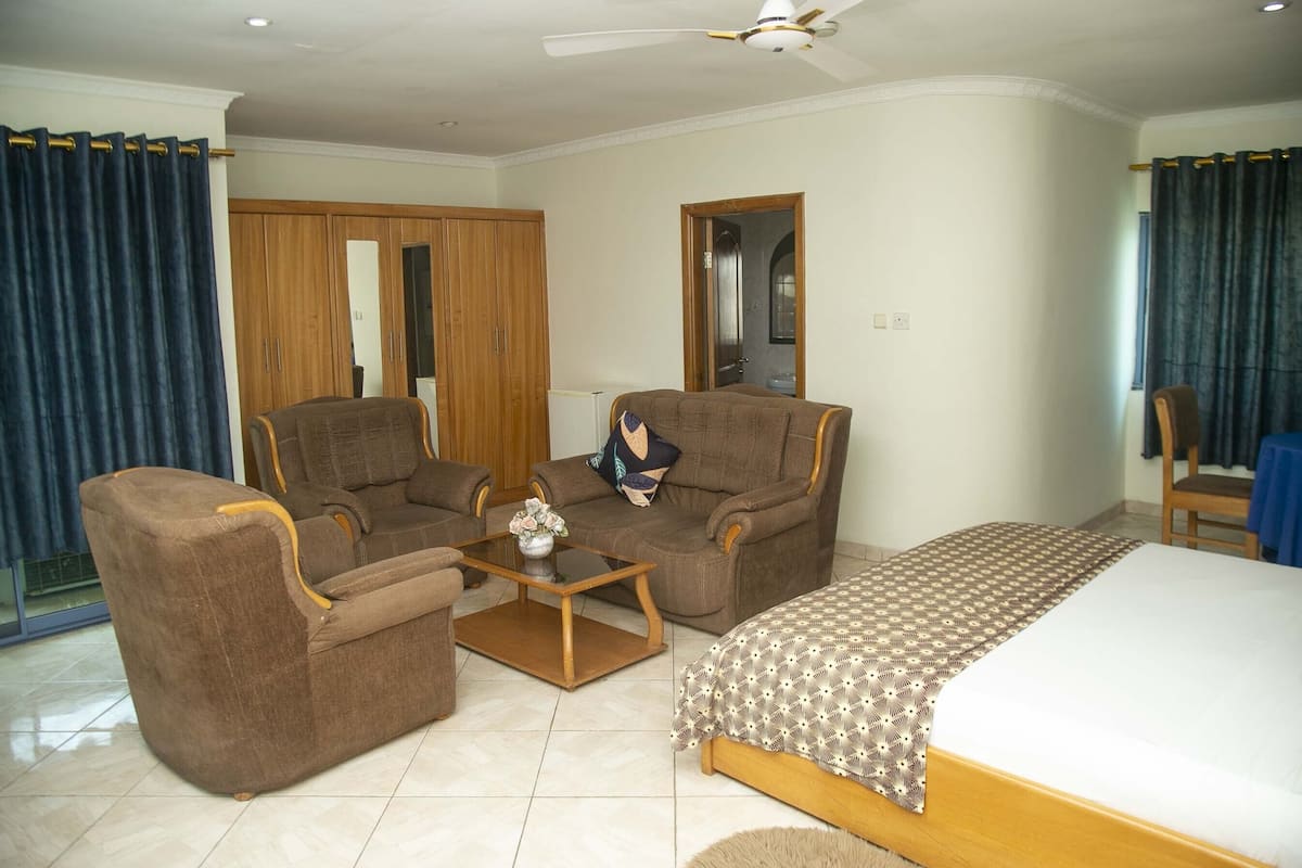 A room with two brown armchairs, a wooden coffee table, a bed with a patterned bedspread, and a ceiling fan.