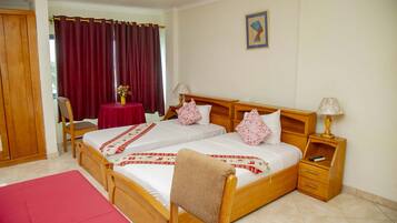 Habitación de hotel con dos camas individuales, un armario de madera, un sofá rojo, una mesita con un florero y un cuadro en la pared.