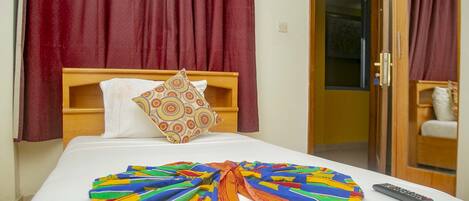 A hotel room with a bed, a colorful blanket, a remote control, and a door leading to a bathroom.