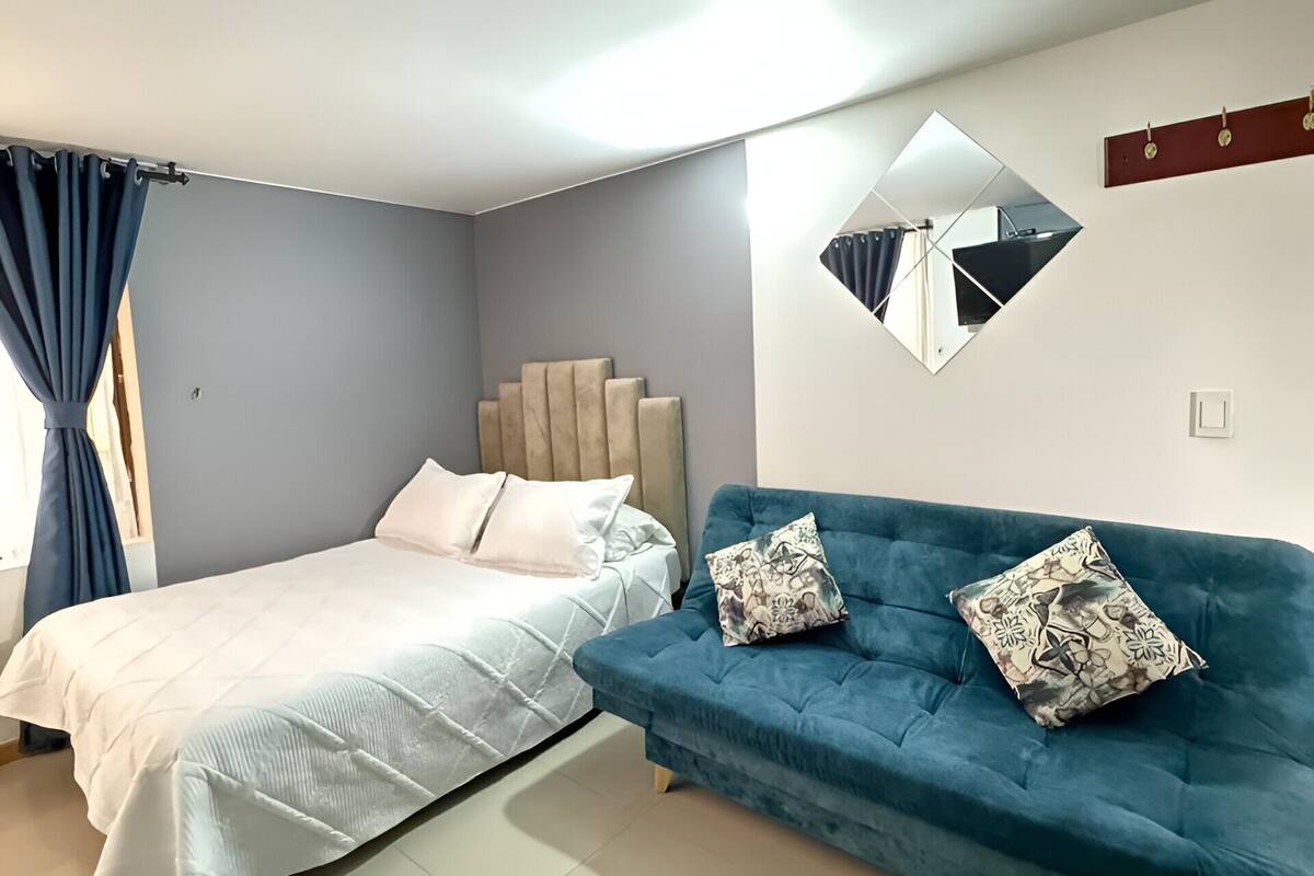 A bedroom with a bed, a blue sofa, a mirror, and a window with curtains.