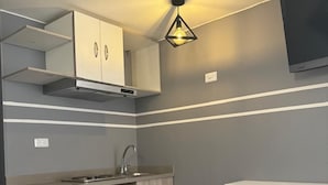 A modern kitchen with a built-in stove, a sink, and a cabinet with a microwave. There is a white trash bin and a shelf on the wall. - Hotel Gran Marquez (Bogotá)