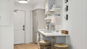 Une cuisine moderne avec des meubles blancs, un plan de travail blanc et deux tabourets.