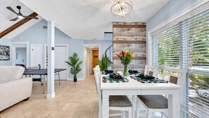 A dining area with a white table set for four, a ceiling fan, and a view through the window blinds.