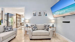A living room with a sofa, two side tables, a flat-screen TV, and artwork on the wall.