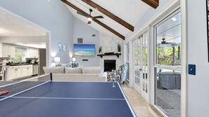 A spacious living area with a ping pong table, a fireplace, and a view of the outdoors.