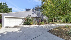 A residential house with a garage, a driveway, and a well-maintained garden with various plants and flowers. - Stunning Lake House w/ Heated Pool + Ping Pong! (Lutz)