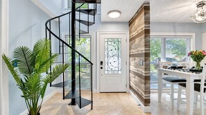 Un intérieur moderne avec un escalier en colimaçon, un coin repas avec une table et des chaises blanches, et une porte ornée de vitraux.