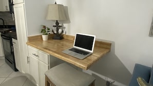 Une cuisine de taille réduite avec des meubles blancs, un plan de travail en bois, un ordinateur portable, une lampe et une petite plante en pot.